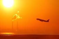 旅行、観光の出発、到着地、東京国際空港を早朝に飛び立つ飛行機のシルエットです。朝焼けでオレンジ色に染まった空に向かって、旅立っていきます。