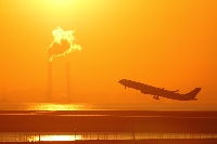 旅行、観光の出発、到着地、東京国際空港を早朝に飛び立つ飛行機のシルエットです。朝焼けでオレンジ色に染まった空に向かって、旅立っていきます。