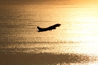 夕日に染まった瀬戸内海の黄金色に輝く海を背景に、離陸していく一機の飛行機のシルエット。道後温泉などの観光でも有名な愛媛県松山市での風景。飛行機用の炭素繊維も松山で作られ、旅行だけでなくビジネス、出張でも飛行機と縁のある場所です